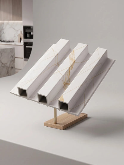 Three white marble-look square-profile metal channel beams with gold veining, displayed on a wooden stand in a modern kitchen setting.